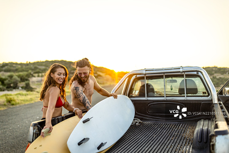 年轻情侣正在皮卡车上装载冲浪板。图片素材