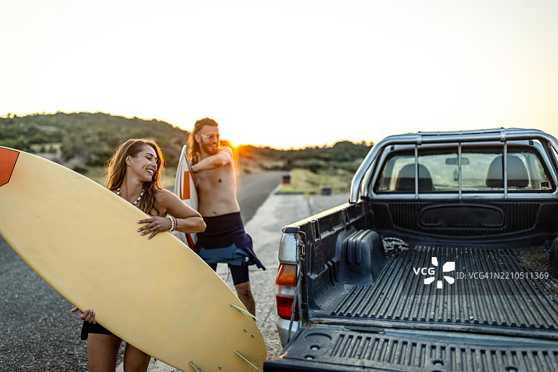 年轻情侣在皮卡车上装载冲浪板。图片素材