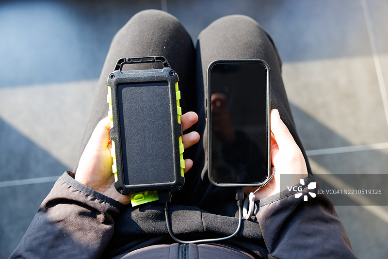 家中停电，一名女性正在使用小型太阳能设备为手机充电。图片素材