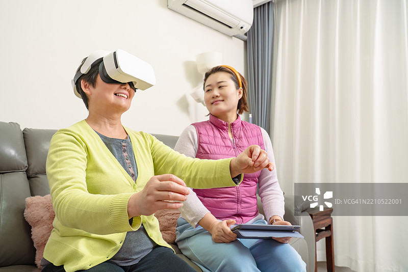 概念虚拟现实技术，亚洲女性正在将平板电脑的图像信号传输到佩戴3D VR眼镜的亚洲老年女性身上。图片素材