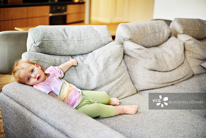 可爱的伤心小女孩在家里的舒适沙发上放松。图片素材