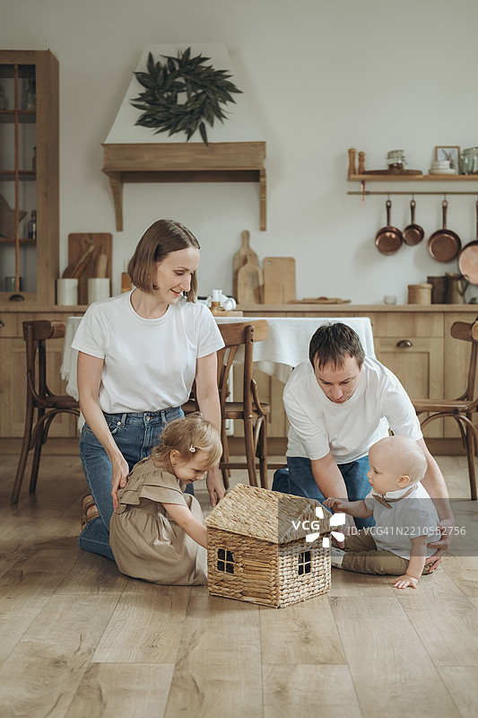 年轻家庭在宽敞的厨房里玩玩具房子。图片素材