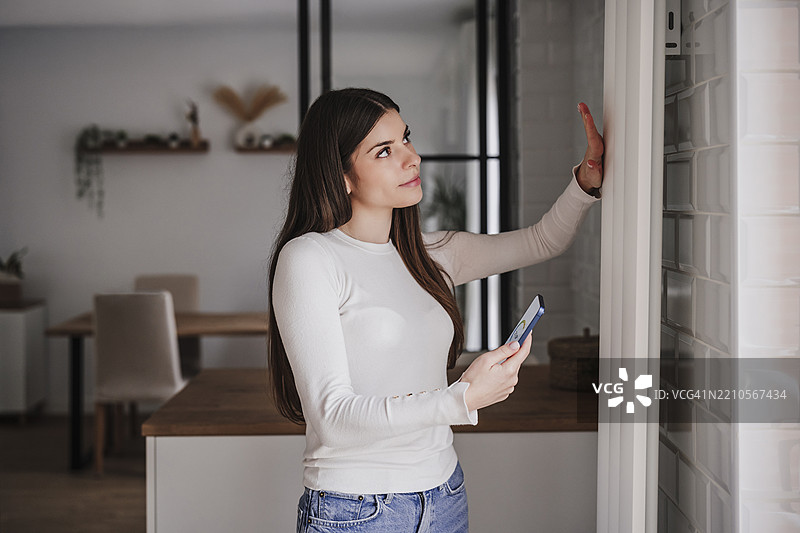 女性使用智能手机应用程序控制家中的暖气。图片素材
