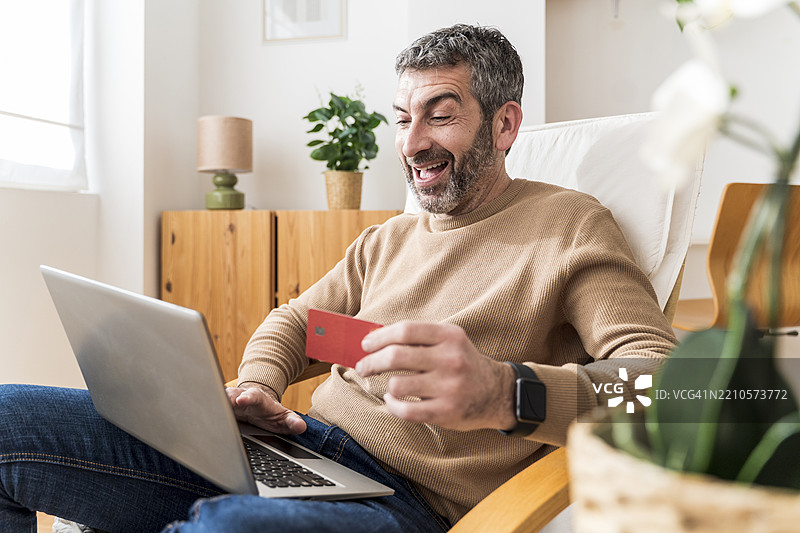 在舒适的客厅里，男人用笔记本电脑和信用卡进行在线购物图片素材