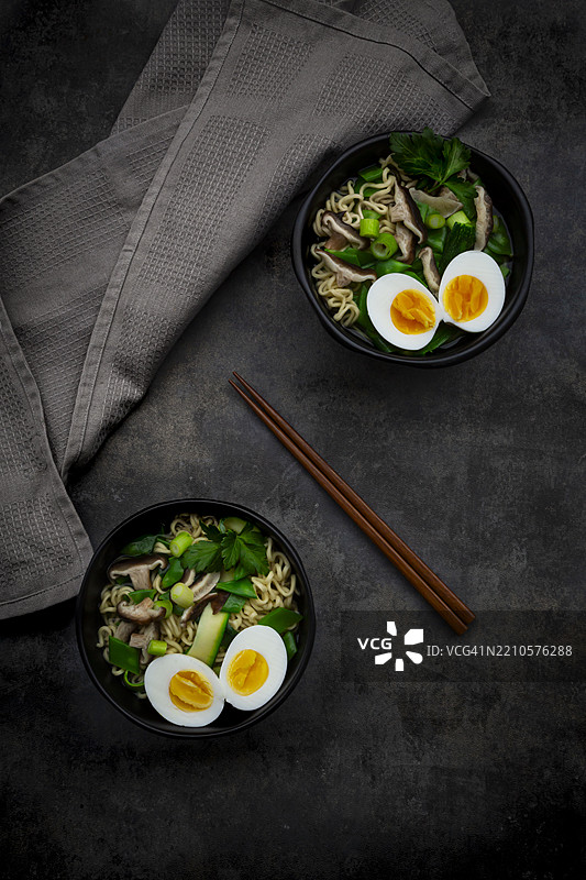 俯视两碗春季拉面的美食，配有鸡蛋、雪豆、 zucchini、葱、香菜和香菇。图片素材