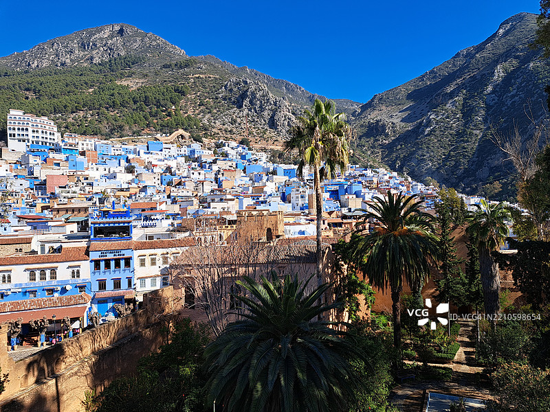 在晴朗的阳光下，色菲沙温的迷人景观中，鲜艳的蓝色建筑依偎在山脉之间。图片素材