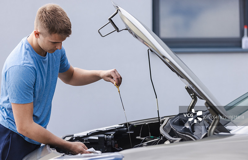 男子在汽车引擎盖下检查油位以进行维护图片素材