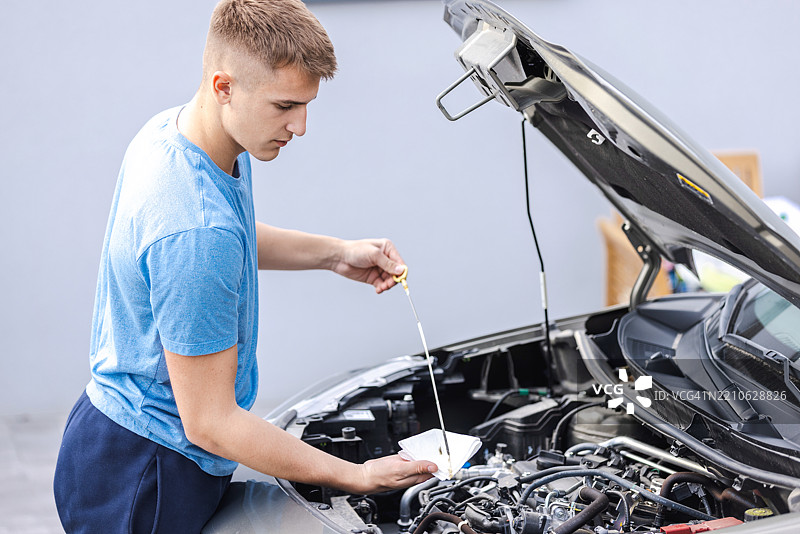 男子在打开的汽车引擎盖下检查机油液位图片素材