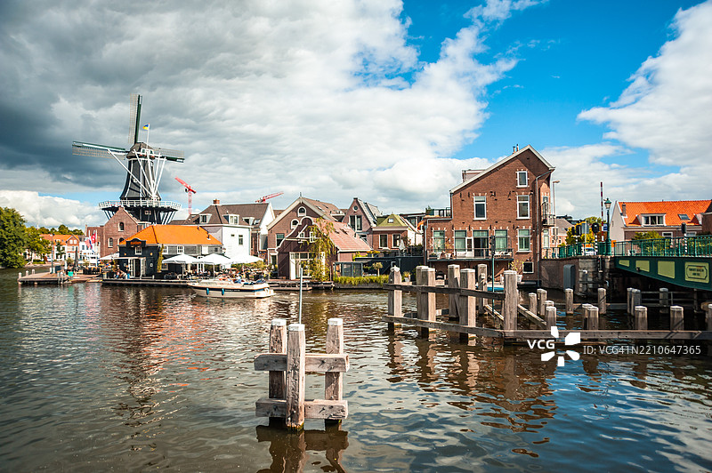 传统荷兰风车旁边有一家餐厅，餐厅外有桌子，面朝运河。图片素材