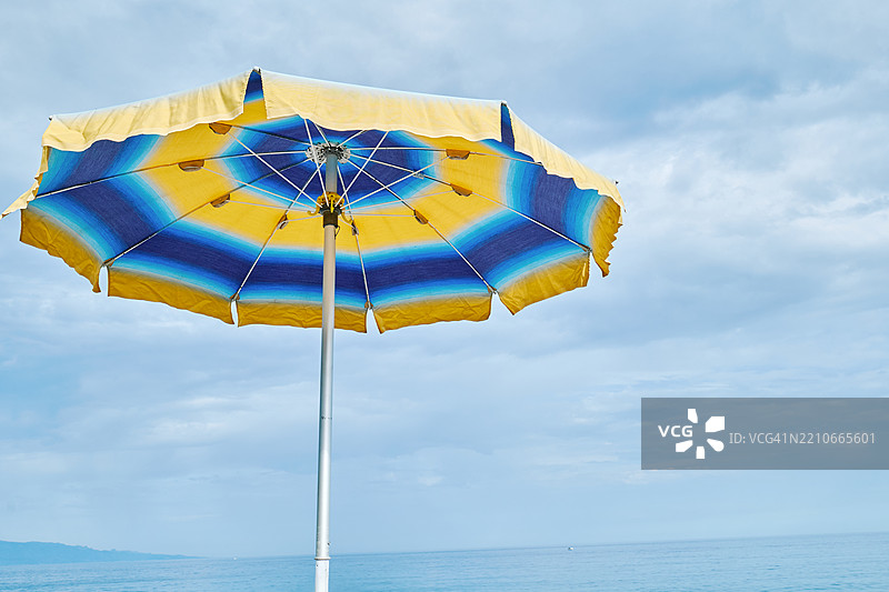 海边蓝黄条纹的沙滩伞在蓝天映衬下图片素材