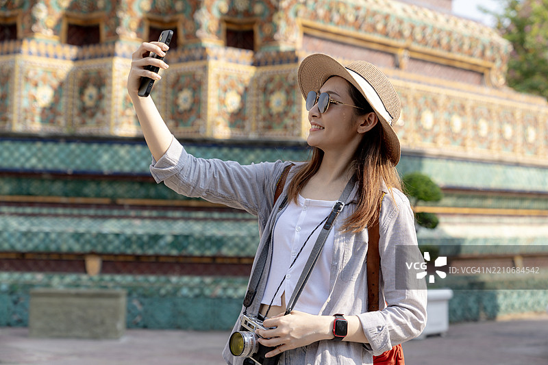 一位年轻女性游客在泰国曼谷探索时用智能手机自拍图片素材