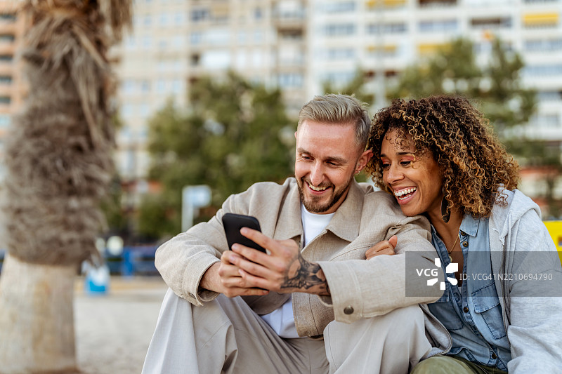 快乐的情侣在户外一起享受看智能手机的时光图片素材