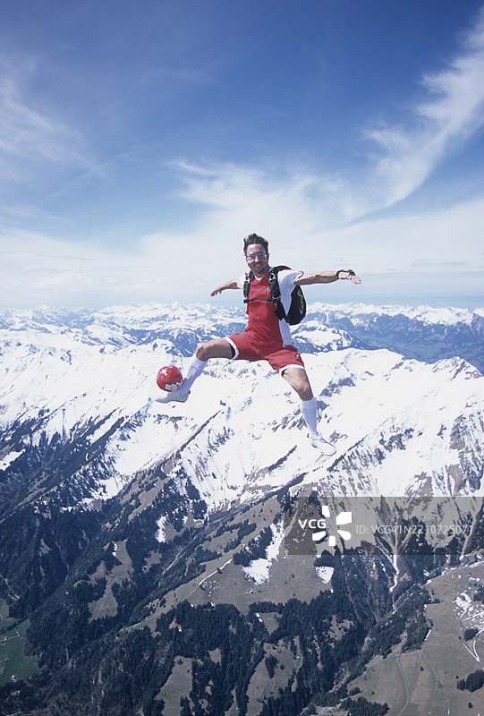 在雪山上空跳伞的运动员与足球图片素材