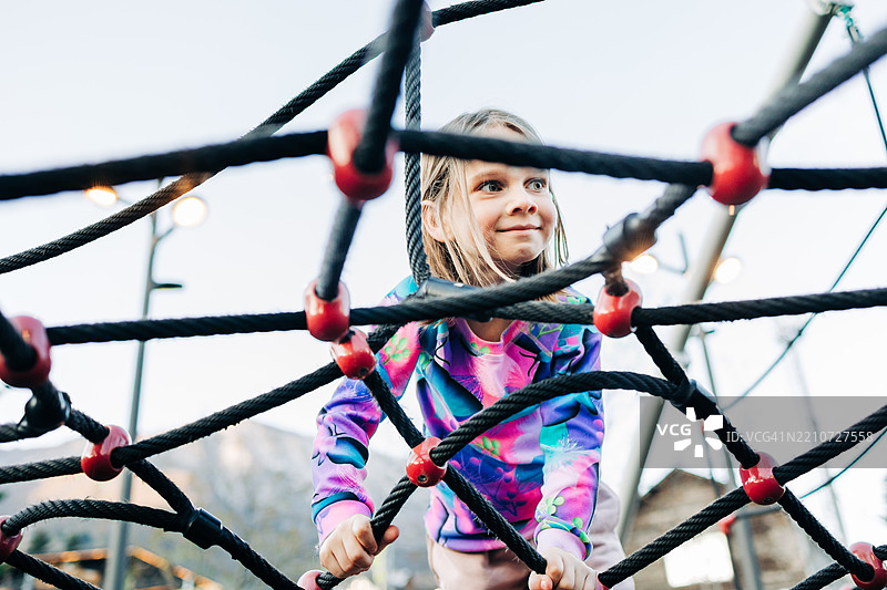 女孩在游乐场攀爬绳网，开心地微笑图片素材