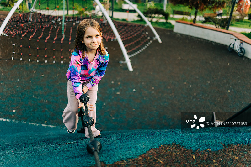 年轻女孩在游乐场的结构上攀爬绳索，展现出决心和力量图片素材