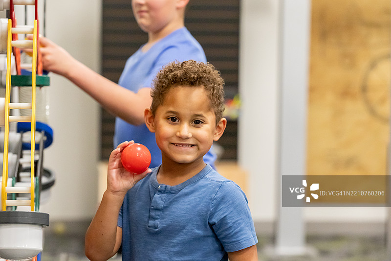 可爱的小男孩在STEM教室里玩教育玩具，同时手里拿着一个球图片素材