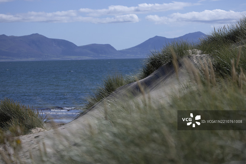 沙丘和海滩俯瞰蓝色海洋和遥远的山脉，位于英国威尔士安格尔西的新堡斯诺多尼亚国家公园。图片素材
