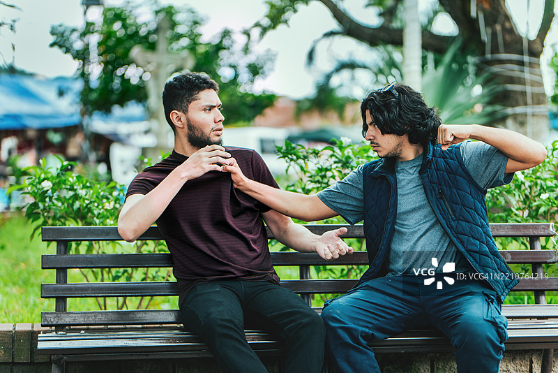 两个男孩在长椅上争论，尼加拉瓜埃斯特利公园的两个男性朋友在长椅上争吵。图片素材