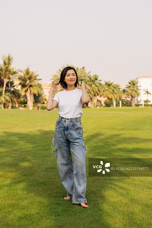 放松的女性站在生机勃勃的草地上，背景是自然风光图片素材