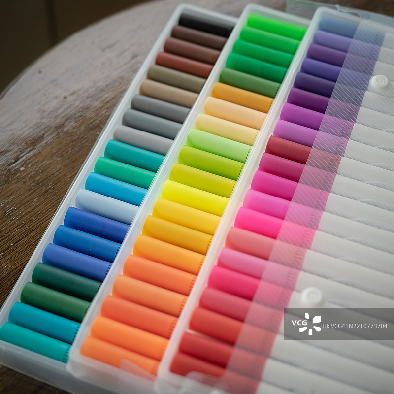 60支彩色马克笔装在透明塑料包装中，背景为木质表面。图片素材