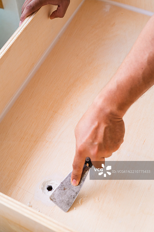 木质表面和手使用刮刀工具刮去的白色油漆图片素材