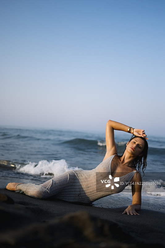 宁静的女性在海浪拍打的沙滩上放松，夕阳西下。图片素材