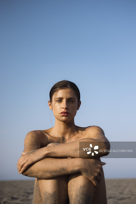 年轻女性坐在沙滩上，皮肤上沾满沙子图片素材