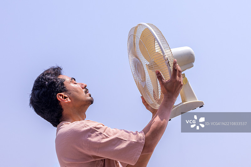 热浪：男子在烈日下用电风扇降温图片素材