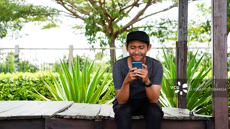 年轻男子在小屋露台上坐着，注视着手机，户外拍摄，科技与自然结合图片素材