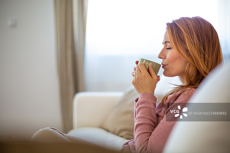 宁静的女性在家中的沙发上享受温暖的饮品图片素材