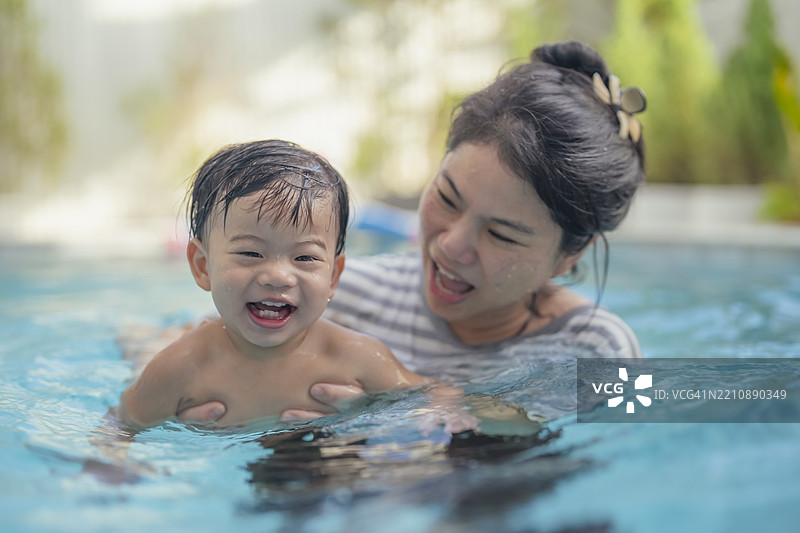 可爱的亚洲幼儿男孩在游泳池中与母亲一起游玩，享受快乐时光。图片素材