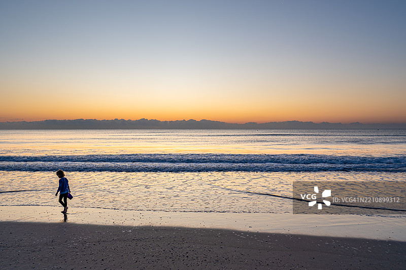 年轻女孩在美国佛罗里达州中部的可可海滩收集贝壳，背景是生机勃勃的春日日出。图片素材