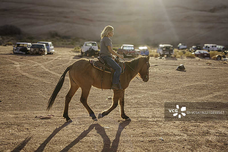 美丽的纳瓦霍女孩在美国西南部亚利桑那州的纪念碑谷附近骑马穿越沙漠图片素材