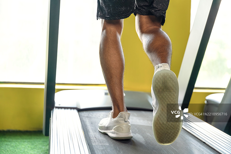 年轻的运动男士在跑步机上跑步，腿部特写。图片素材