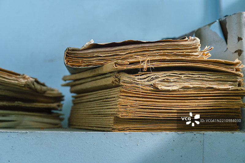 陈旧、磨损的文件堆放在蓝色背景的昏暗房间的架子上图片素材