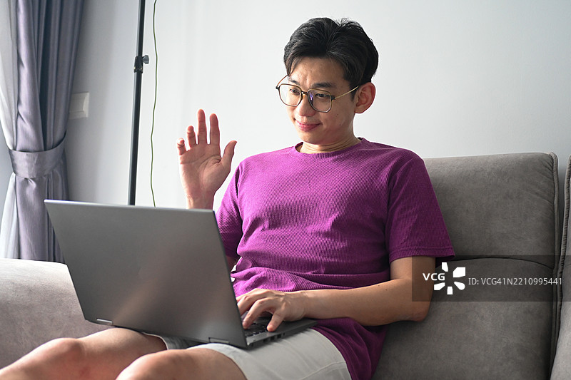 专注的马来西亚专业人士在家远程办公，舒适地坐在沙发上使用笔记本电脑，分析数据并为他的远程团队提供见解。图片素材