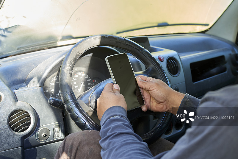 专业送货司机在驾驶商用车辆时使用智能手机，代表着危险的分心驾驶行为，危及道路安全。图片素材