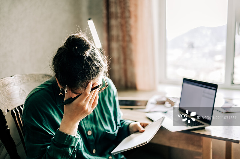 中年女性在家工作，感到压力，正在阅读笔记。图片素材