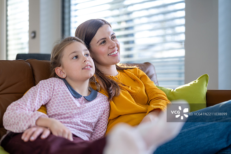 快乐的母女穿着休闲服装，在棕色沙发上享受电视时光图片素材