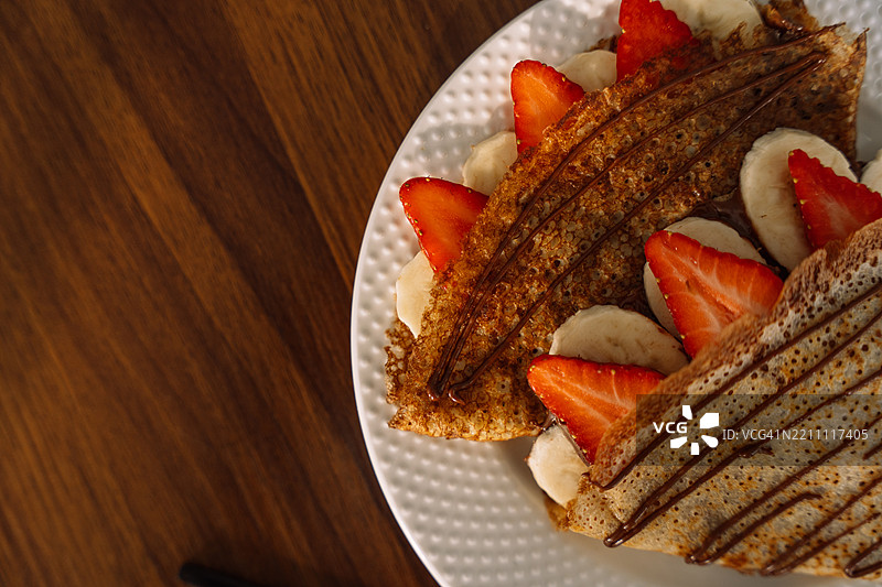 薄煎饼配草莓和香蕉，淋上巧克力糖浆，折叠成三角形图片素材