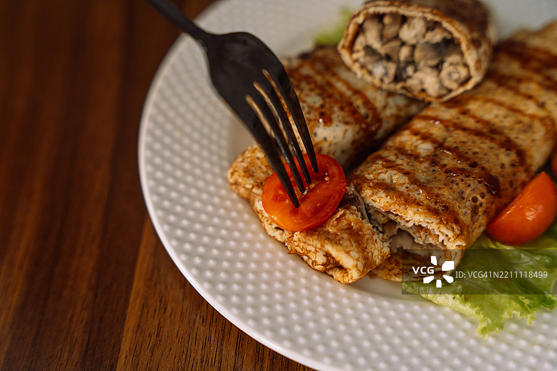 木桌上的盘子里放着薄饼，里面包裹着肉馅。图片素材