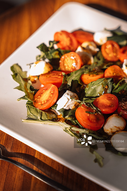 白色圆盘中的沙拉，配有马苏里拉奶酪、樱桃番茄和生菜，旁边放着一把叉子。图片素材