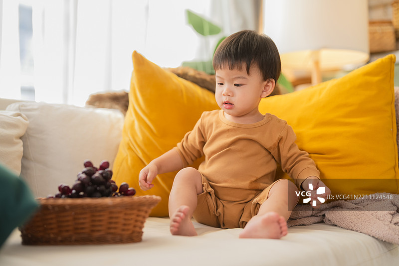 可爱好奇顽皮的亚洲幼儿（18-23个月）坐着放松，微笑着，展现出愉快美好的家庭生活理念。图片素材