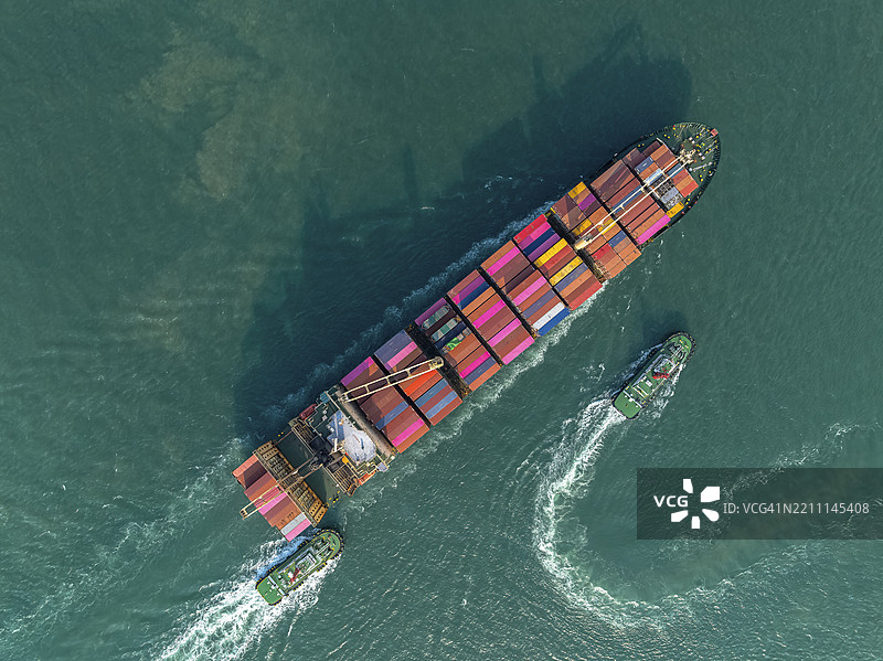 航拍俯视，拖船正在将散货集装箱船推入港口。商业贸易物流和国际运输，进口、出口通过集装箱货船。图片素材