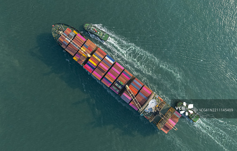 航拍视角，拖船正在将散货集装箱船推入港口。商业贸易物流和国际运输，进口、出口通过集装箱货船。图片素材