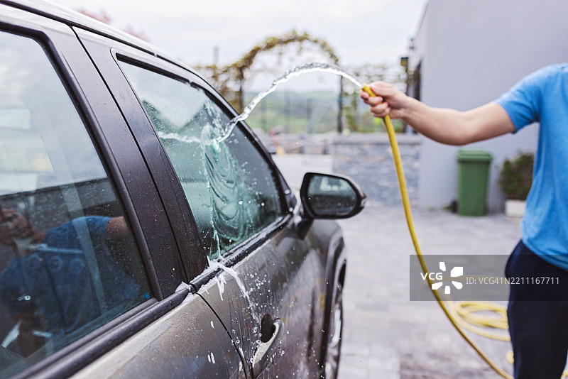 在阳光明媚的日子里，人在户外用水管洗车图片素材