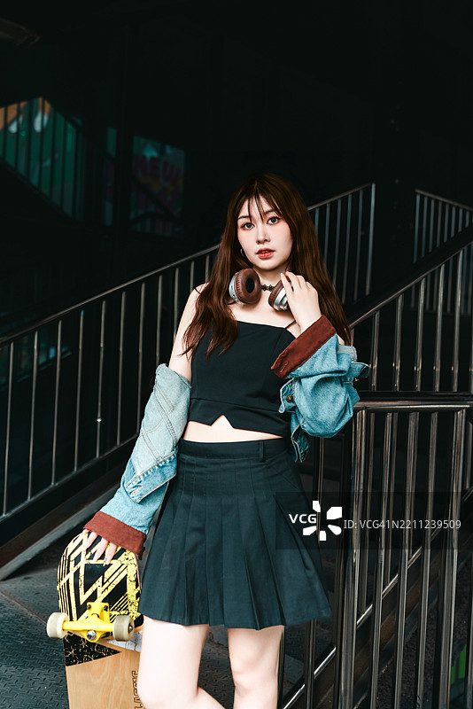 城市滑板女孩站在台阶上，手里拿着滑板。图片素材