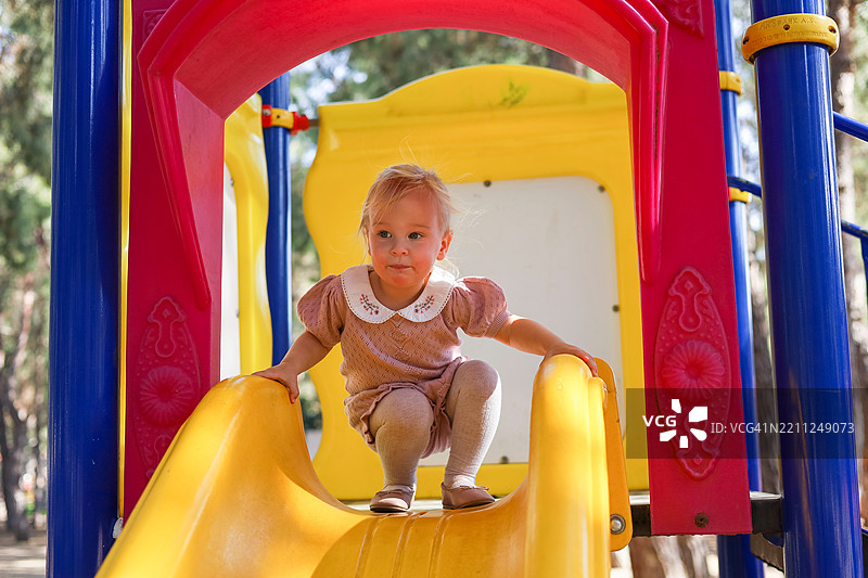 一个快乐的小女孩微笑着准备在五彩斑斓的游乐设施上滑滑梯。图片素材
