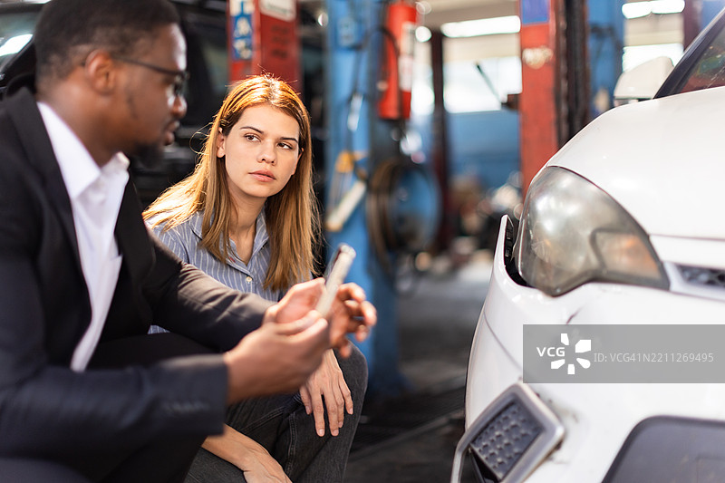 汽车保险索赔评估官审查并考虑汽车事故评估。保险代理人与一位面临汽车问题的女性签署合同，索赔调整员处理汽车损坏。图片素材
