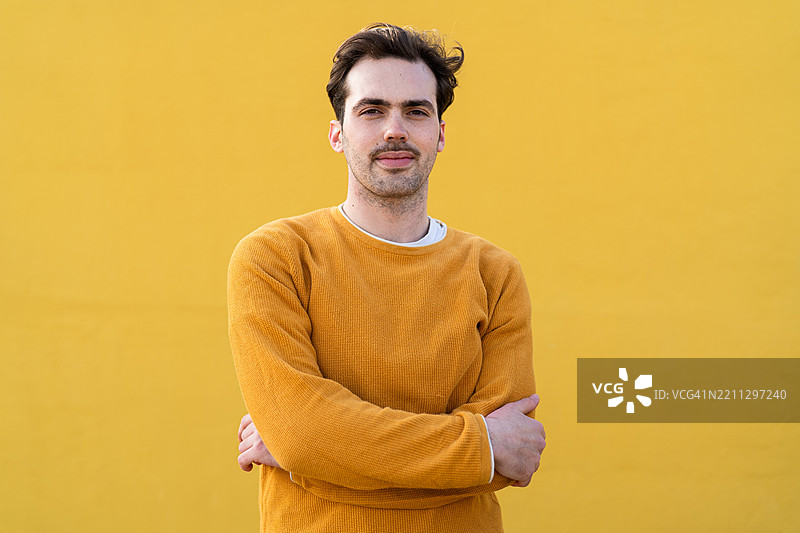 年轻男子微笑着，双臂交叉在黄色背景前图片素材